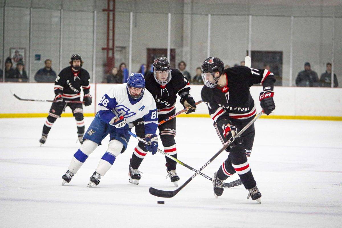 One hockey player wearing a GVSU uniform skates alongside three hockey players wearing Davenport uniforms
